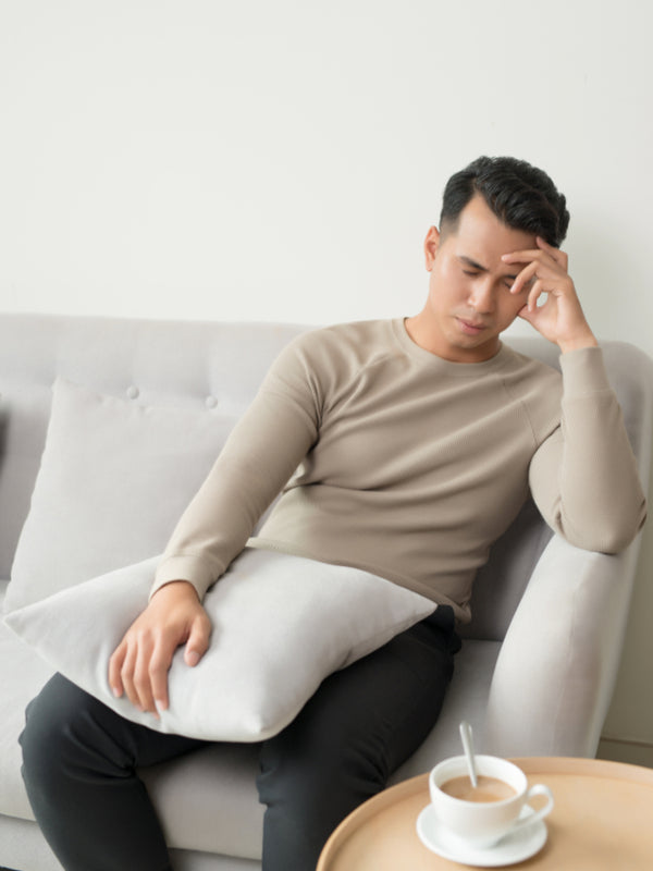 Tired, sleepy man sitting on the sofa holding pillow in his lap