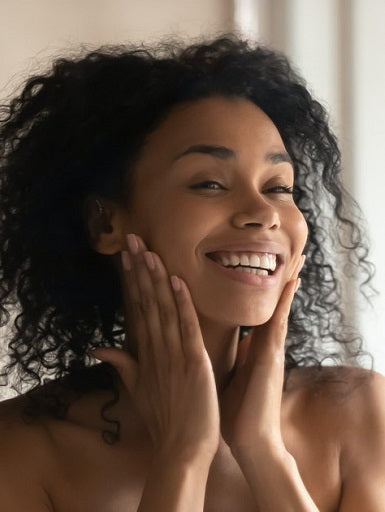 Beautiful afro-american girl looking at her healthy skin in the mirror