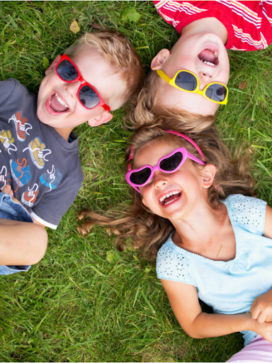 Three laughing kids lying on the grass wearing colorful sunglasses